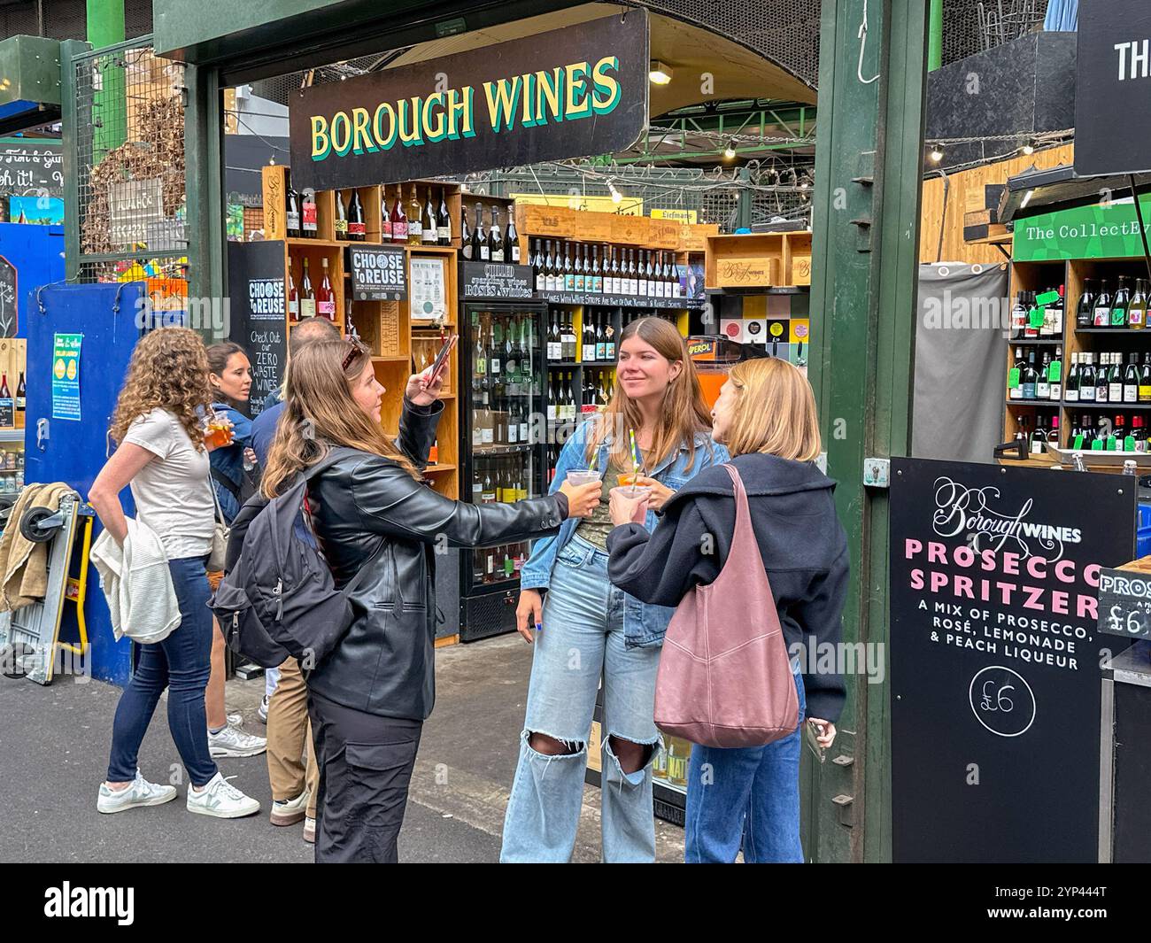 London, England, UK - 3 July 2024: People posing with drinks outside a wine stall at Borough Market in central London - Smartphone Captured Stock Image
