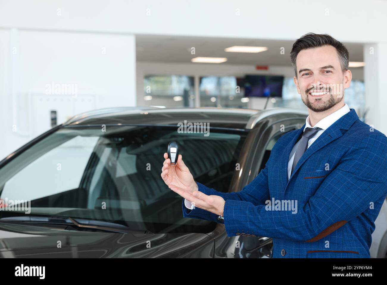 Happy salesman holding key near new black car in salon Stock Photo - Alamy
