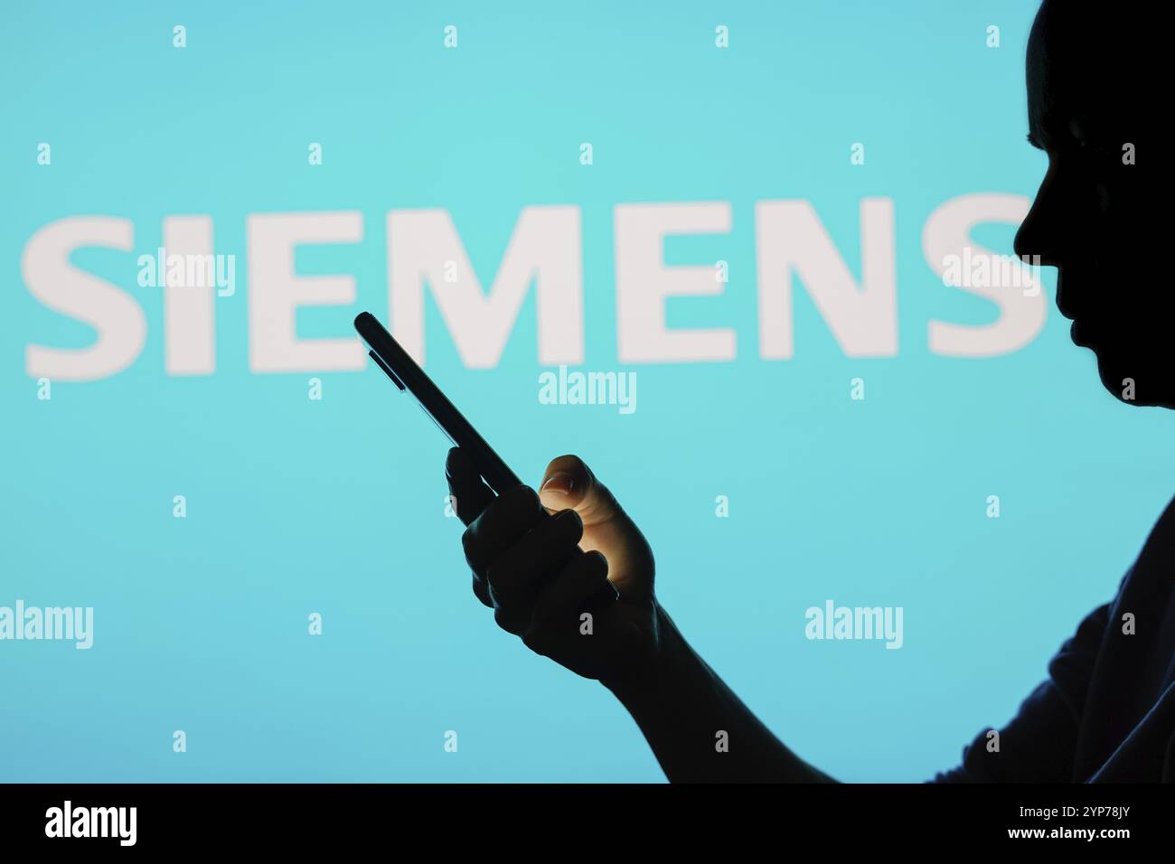 In this photo illustration, the Siemens logo is seen in the background of a silhouetted woman holding a mobile phone Stock Photo