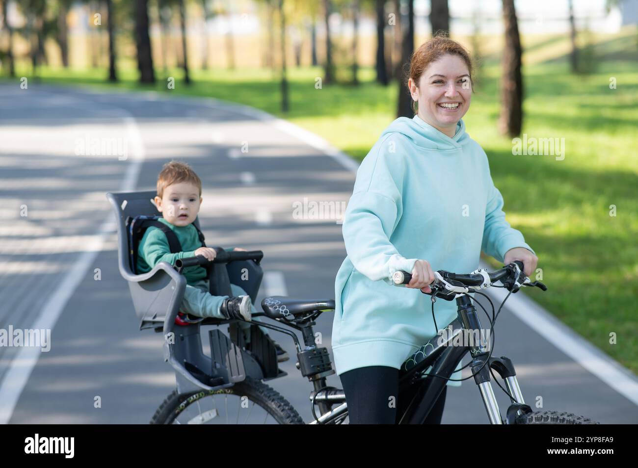 Caucasian woman riding a bicycle with her toddler son sitting behind ...