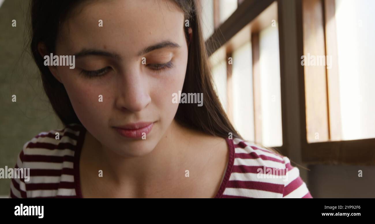 Front view close up of a teenage Caucasian girl sitting by a window ...
