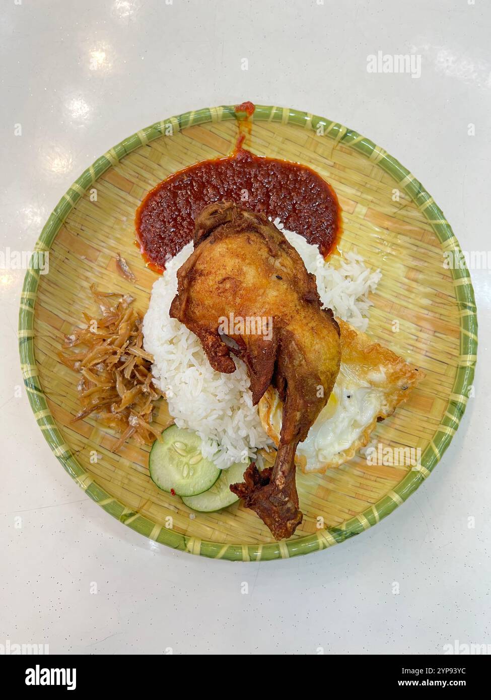 A plate of well presented Nasi Lemak, chicken drumstick, sambal sauce, fried egg, fried ikan bilis, coconut rice, fresh cucumber. Malaysia culinary Stock Photo
