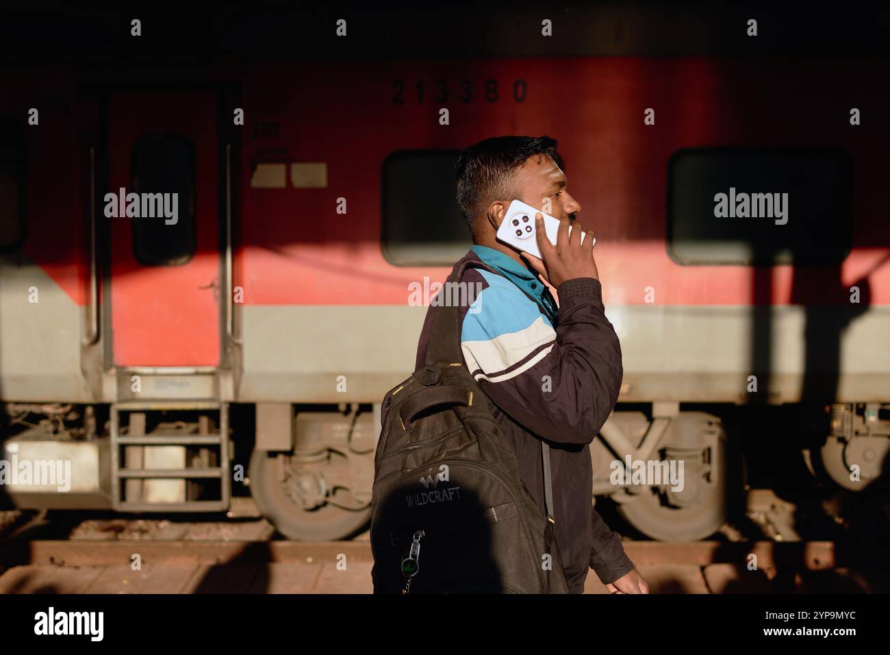 A young Indian man at Dadar Station in Mumbai, India, talking on his mobile phone, with a train in the background Stock Photo