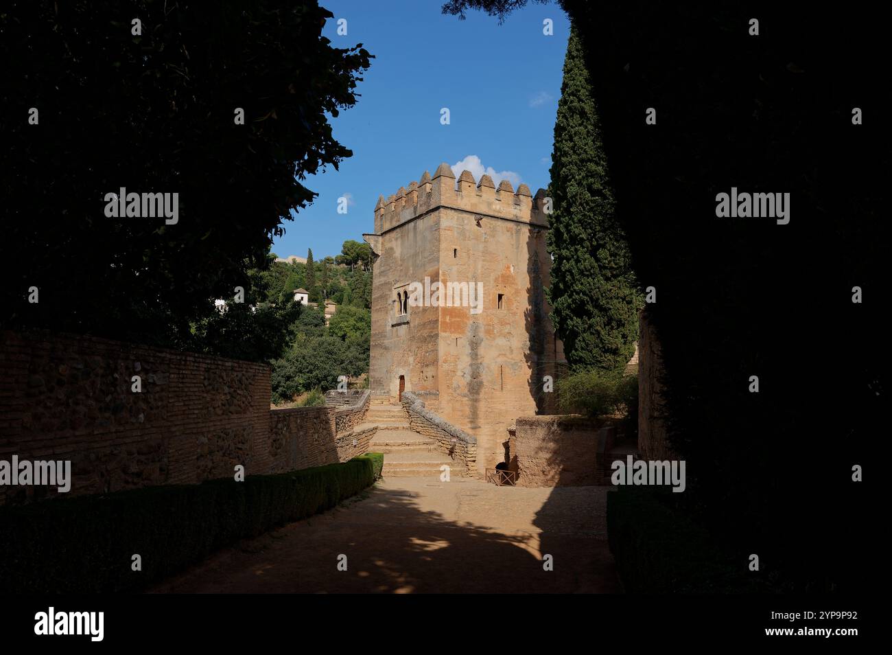 A historic tower in the Alhambra of Granada, framed by shaded pathways ...