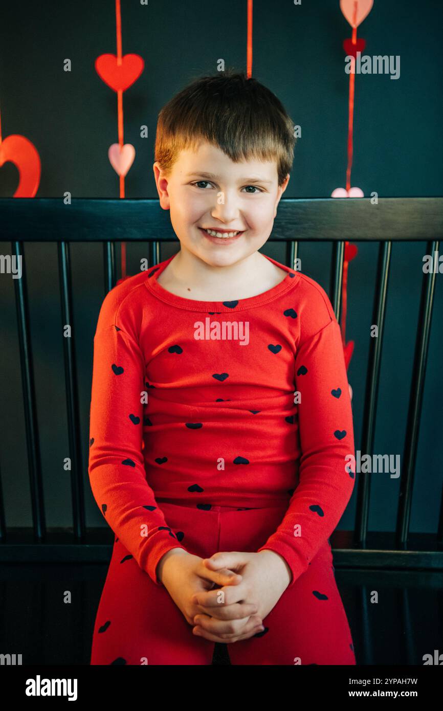Smiling boy in red heart-pattern pajamas sitting on a black bench Stock ...