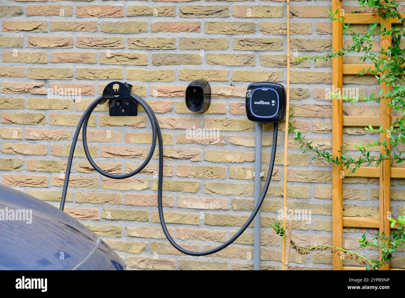 August 18, 2022 - Hoogeveen, Netherlands: EV and charger mounted on a yellow brick wall, symbolizing sustainable energy solutions and the growing tren Stock Photo