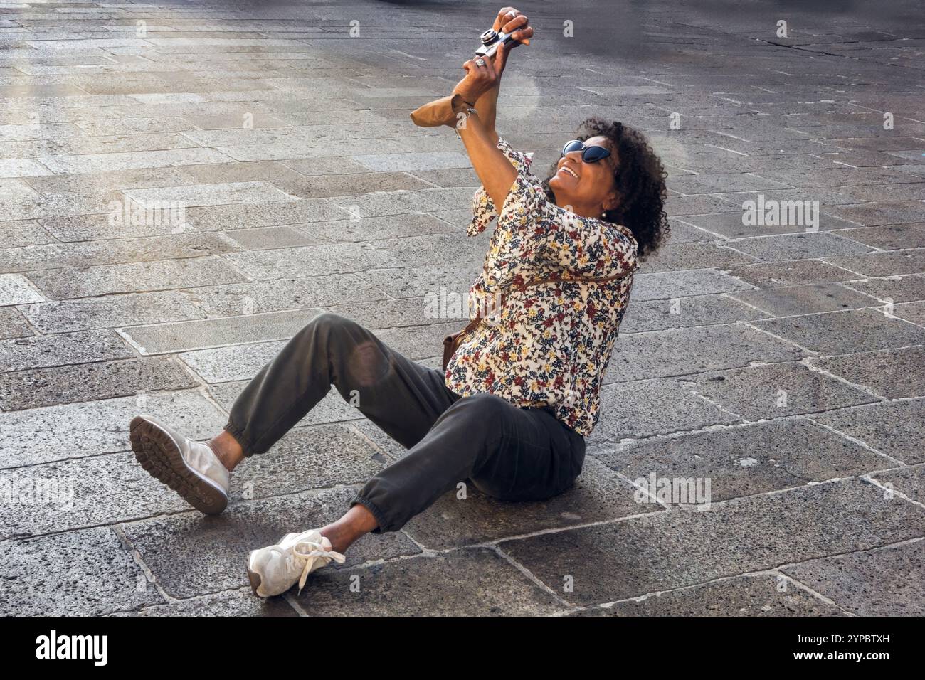 Smiling South American tourist, taking a photo while sitting on the ground to better frame the picture. Stock Photo