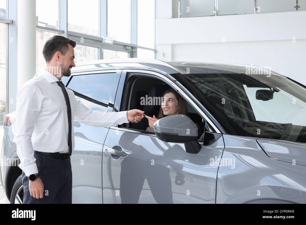 Woman giving key to man inside new car in salon Stock Photo - Alamy