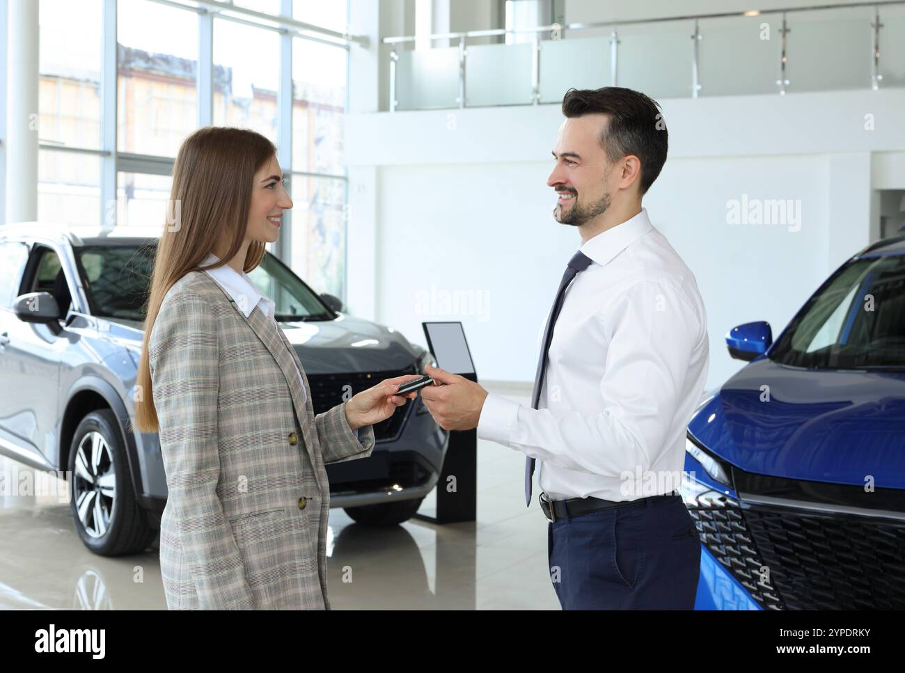 Saleswoman giving key to client near new car in salon Stock Photo - Alamy