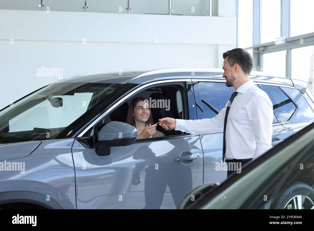 Woman giving key to man inside new car in salon Stock Photo - Alamy