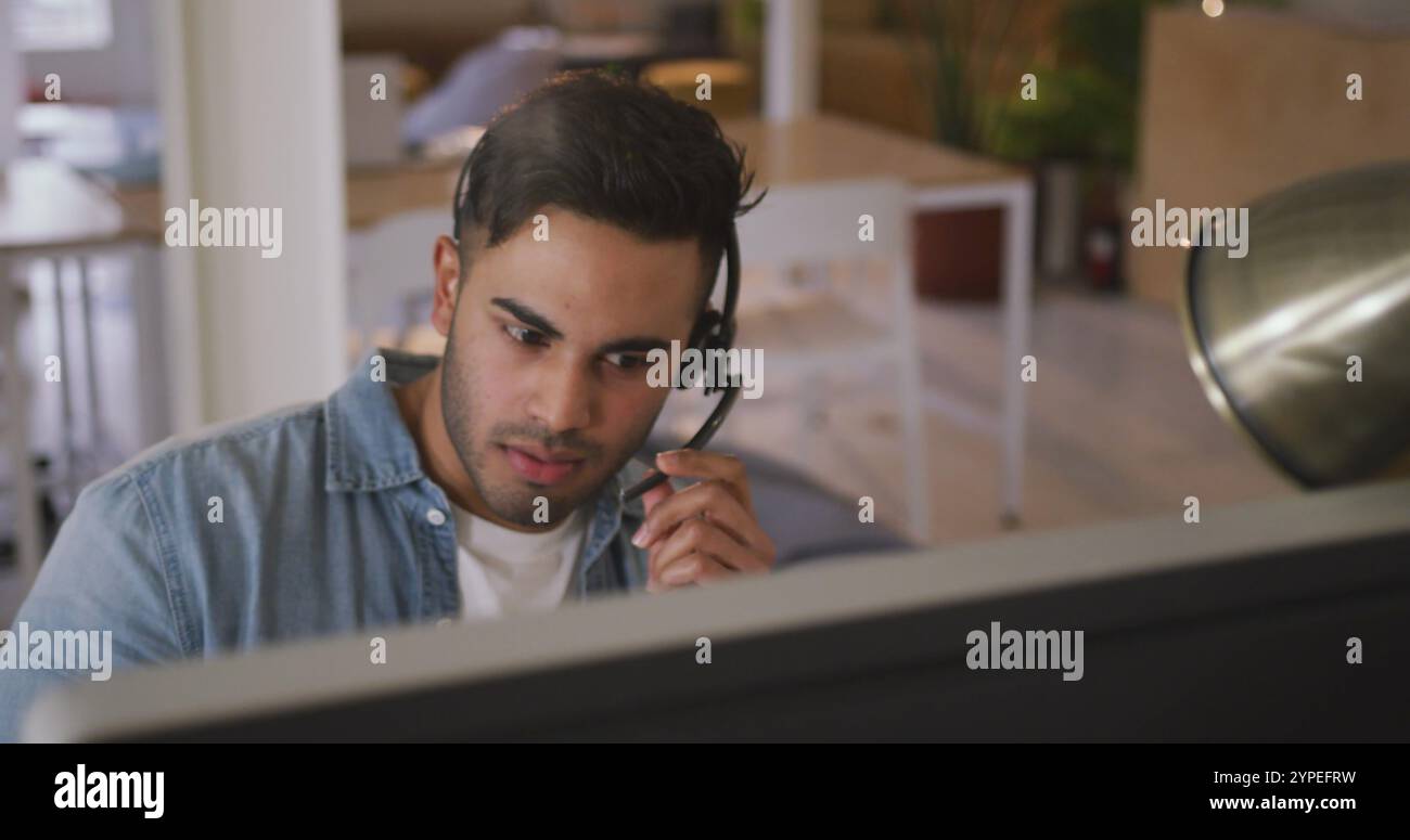 Front view of a happy biracial man working in a creative office, wearing headset, talking and smilin Stock Photo