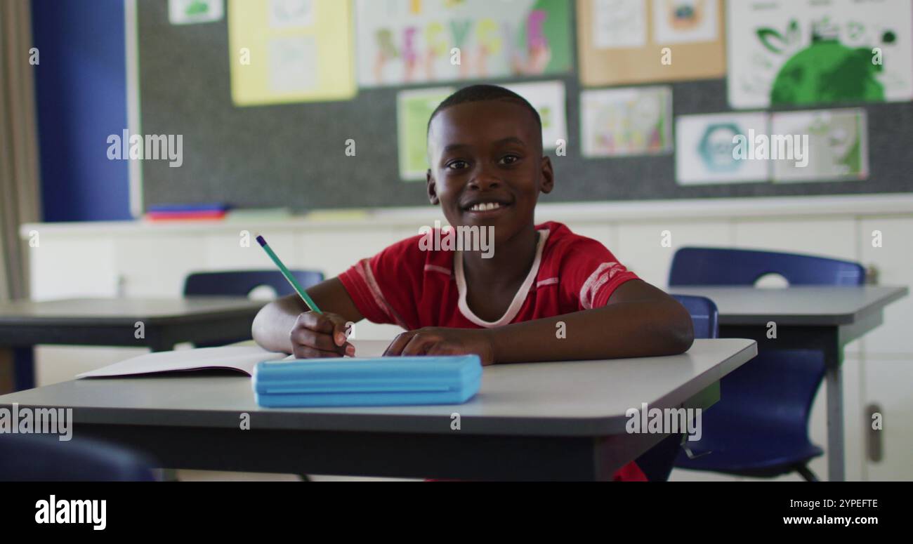 Portrait of happy african american schoolboy sitting at classroom ...
