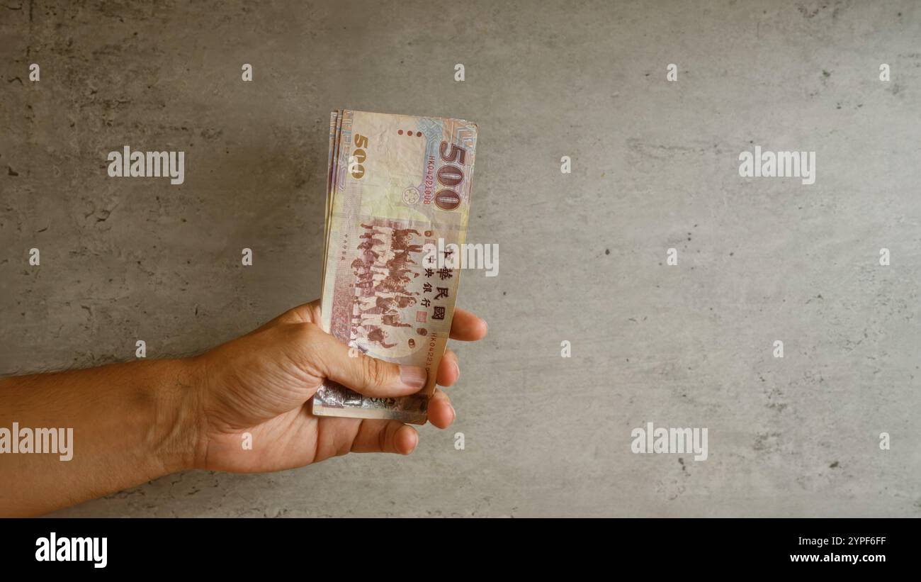 hand-holding-taiwanese-dollars-against-concrete-wall-background