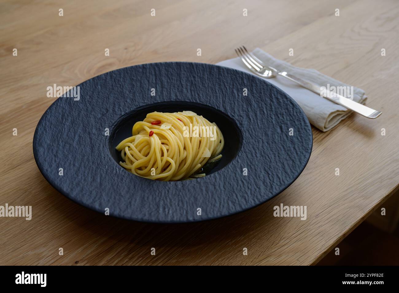 Spaghetti Colatura di Alici with Garlic and Peperoncini on a Black Plate Stock Photo