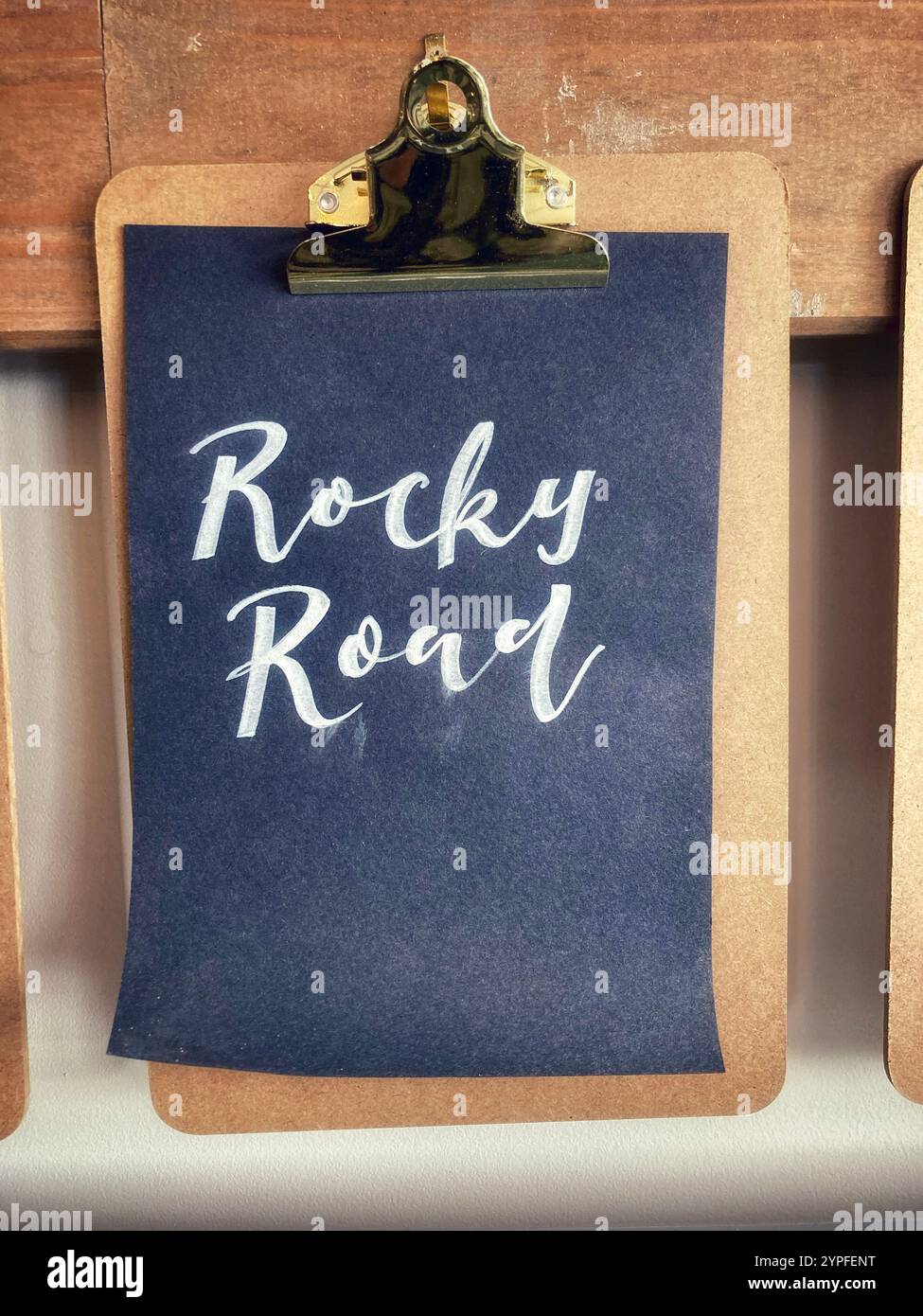 A black sheet of paper with white handwriting on a clipboard saying "Rocky Road" - Smartphone Captured Stock Image