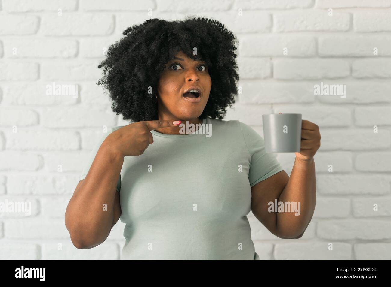 Shock Realisation African American surprised woman holding a gray mug while pointing at ...