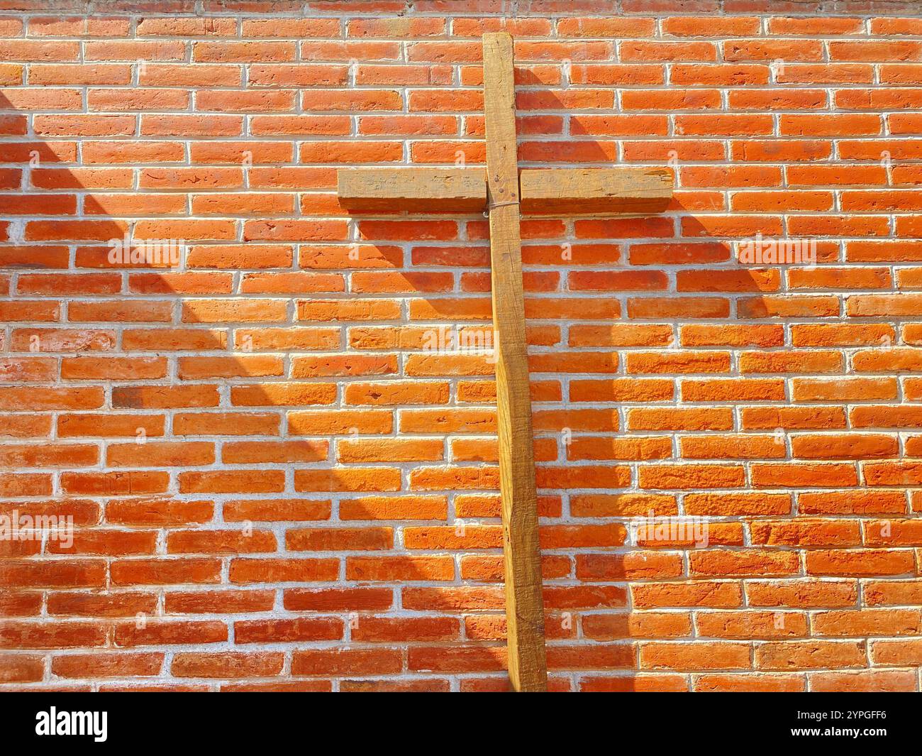 A wooden Catholic cross in front o f a red bricks wall in a patio in San Miguel de las Tetillas, Villa Progreso, Ezequiel Montes, Queretaro, Mexico - Smartphone Captured Stock Image