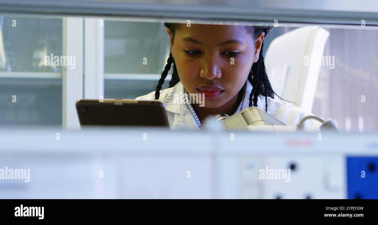 Scientist looking through microscope while using digital tablet in laboratory Stock Photo