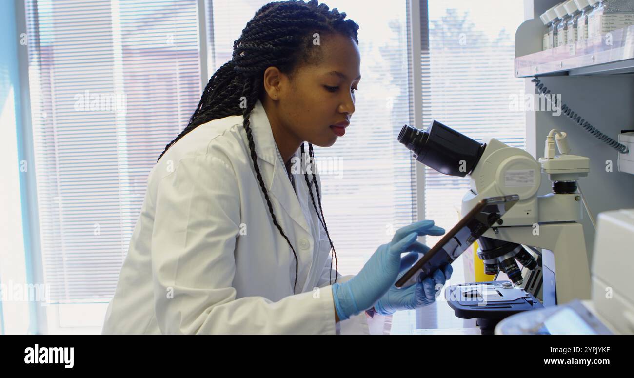 Scientist looking through microscope while using digital tablet in laboratory Stock Photo