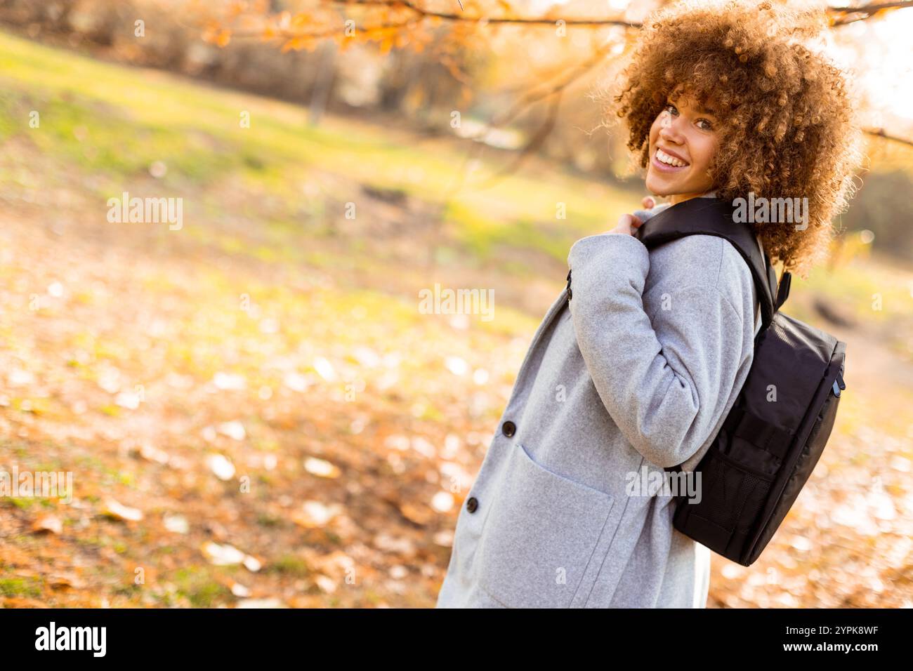 In a beautiful autumn park, a joyful young woman with curly hair ...