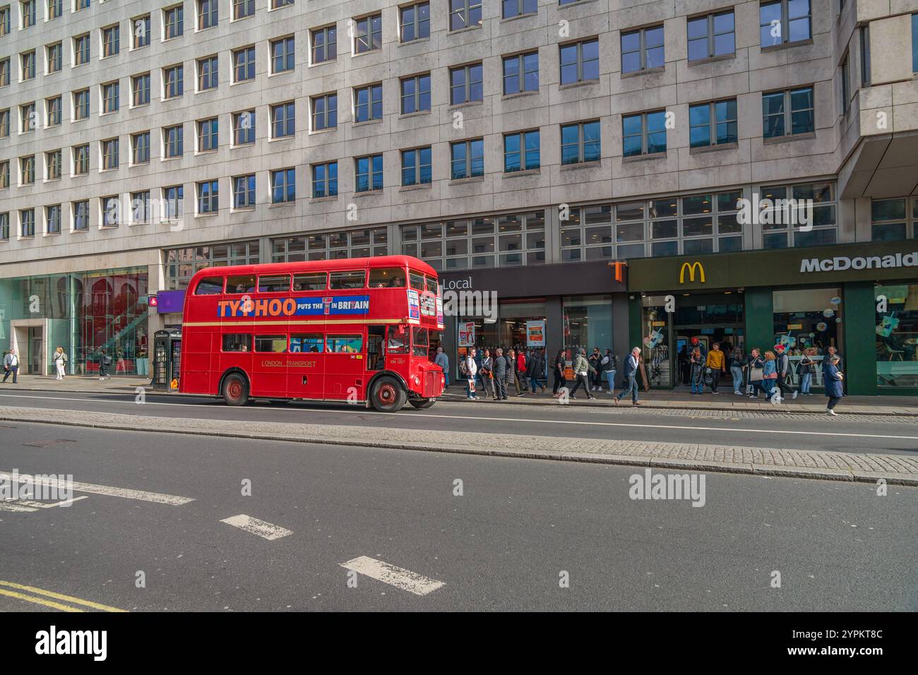 Vintage red Routemaster tourist bus passes McDonalds restaurant with queue of customers outside on busy London street Stock Photo