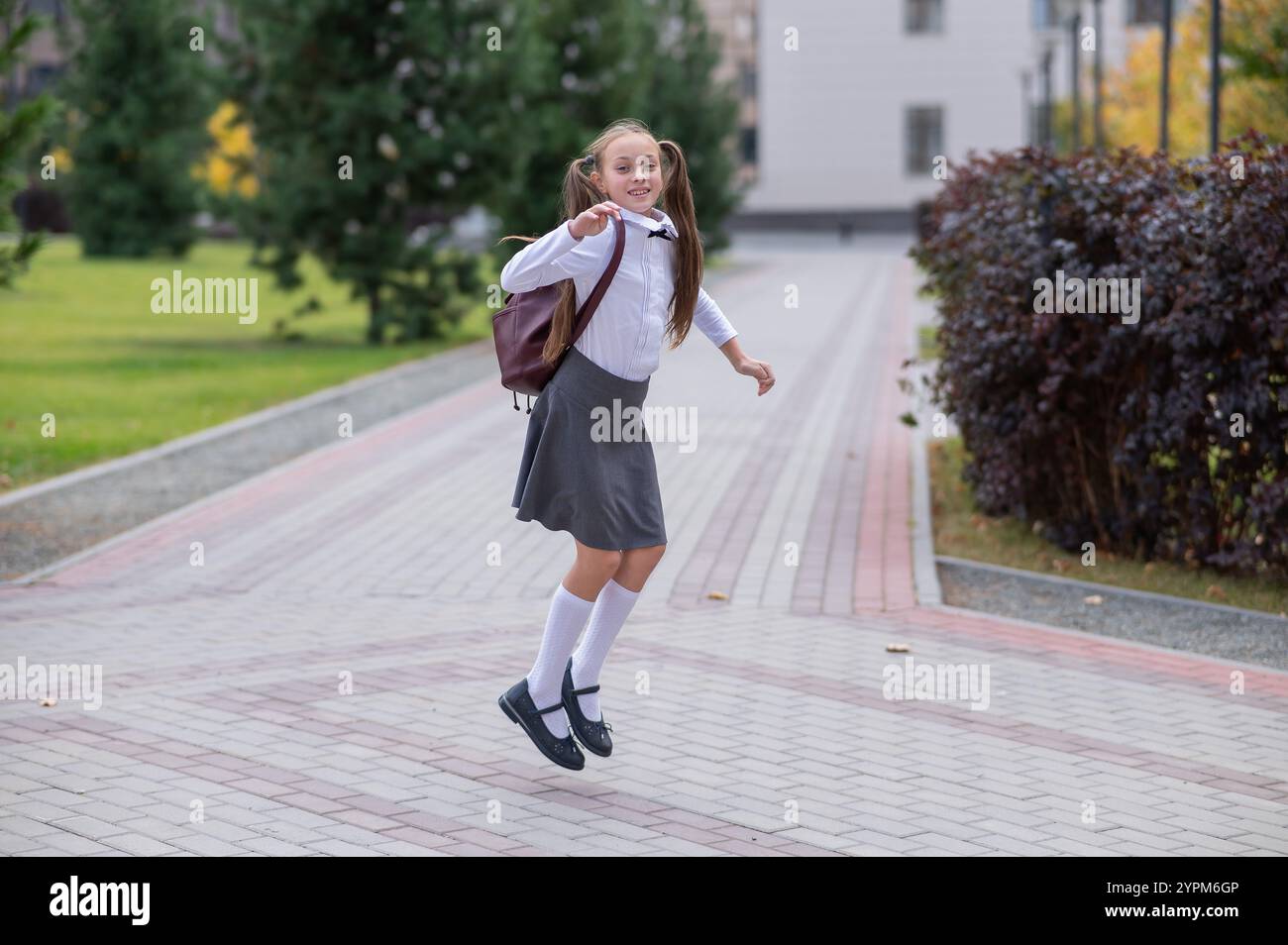 Happy caucasian girl in uniform and with a backpack jumping outdoors ...