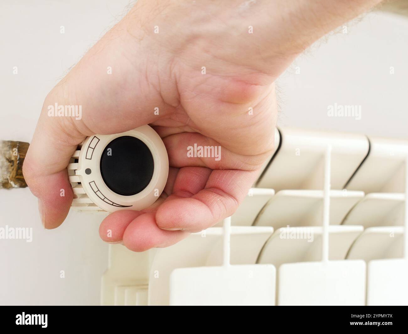 A close-up of a hand turning the thermostat knob on a radiator heater ...