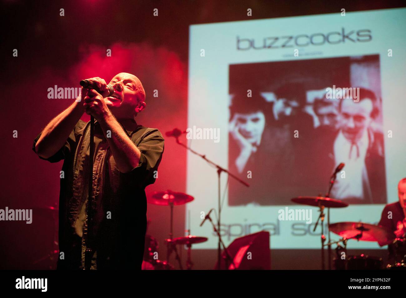 Howard Devoto singing at The Buzzcocks reunion concert, Manchester Apollo, 25 May 2012. The bands debut EP, 'Spiral Scratch', is seen projected behind. Stock Photo