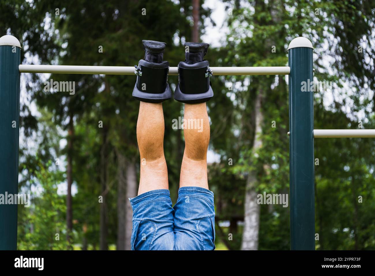 A mans legs in gravity boots hangs on a horizontal bar outdoors on a ...