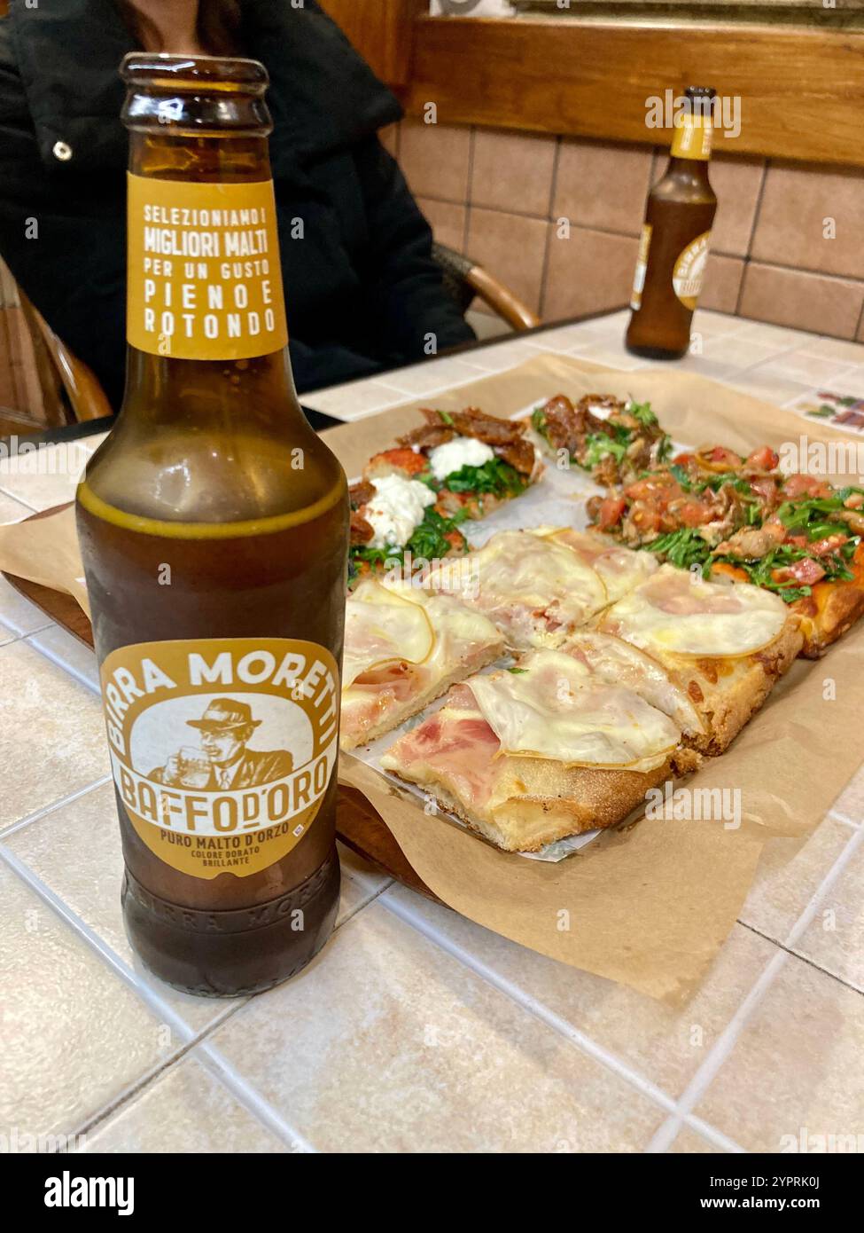 Two bottles of birra moretti Baffo d'oro and pizza on a tile table in a restaurant - Smartphone Captured Stock Image