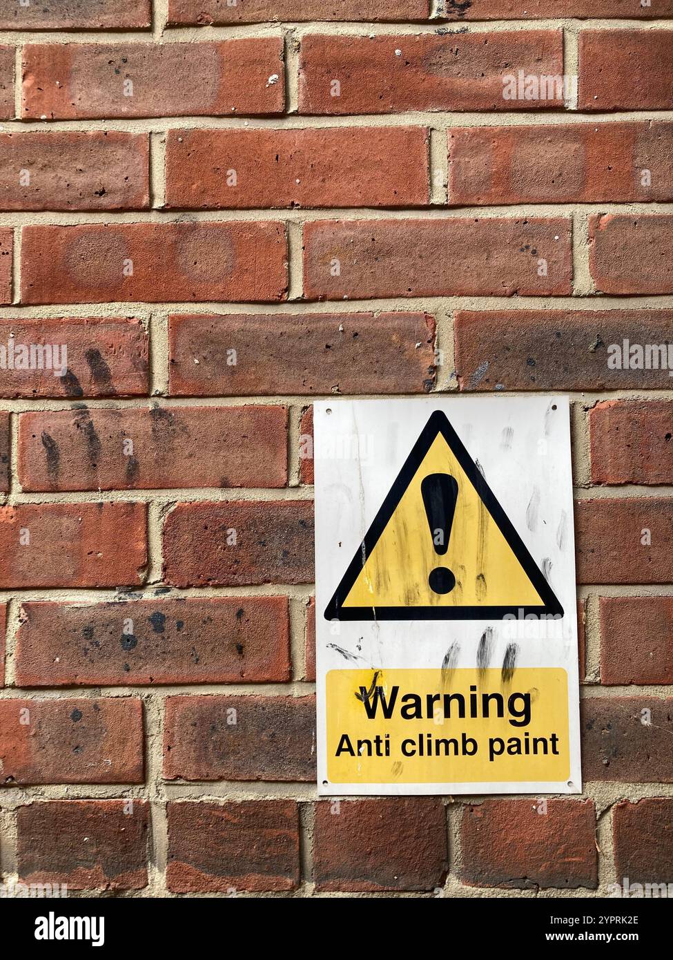 A warning sign on a red brick wall advising the use of Anti-climb paint, on the sign and on the wall are black finger streaks - Smartphone Captured Stock Image