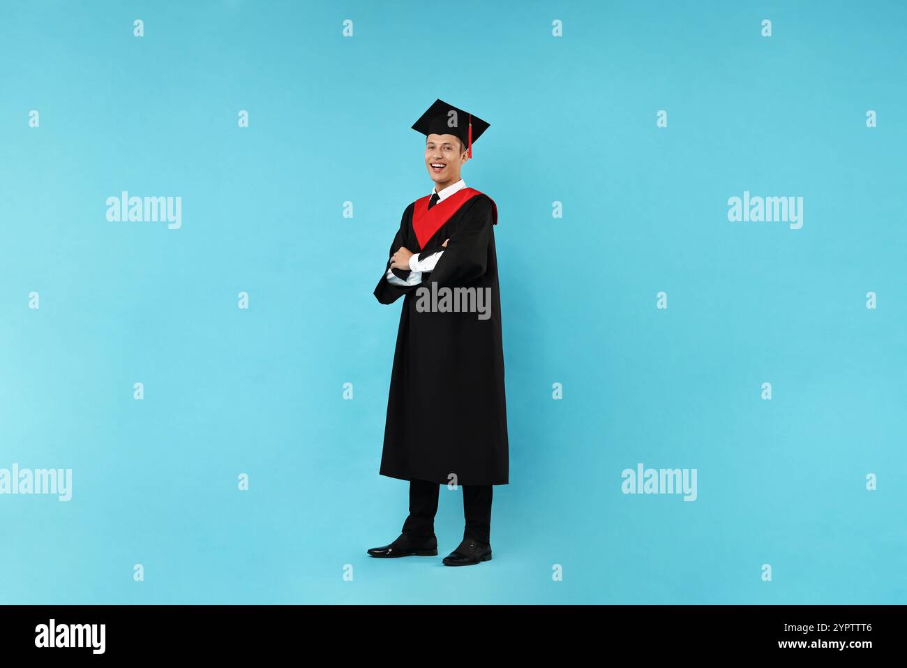 Happy student with crossed arms after graduation on light blue ...
