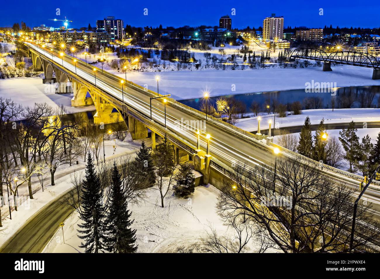 A bridge over a river with a city in the background. The bridge is lit up at night, creating a warm and inviting atmosphere Stock Photo