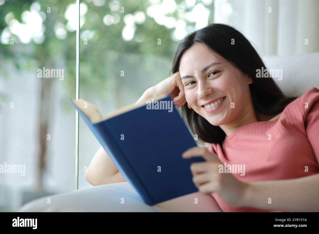 Happy asian reader holding paper book looking at you at home Stock Photo