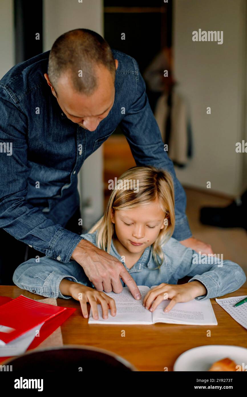 Father helping son doing homework while sitting near table at home Stock Photo
