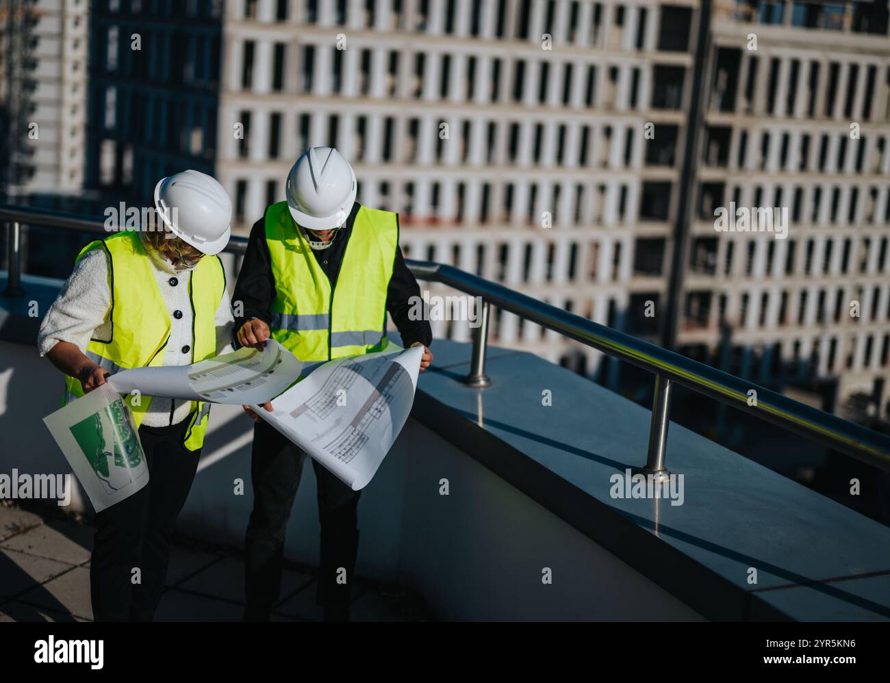 Architects discussing blueprints on rooftop of urban construction site ...