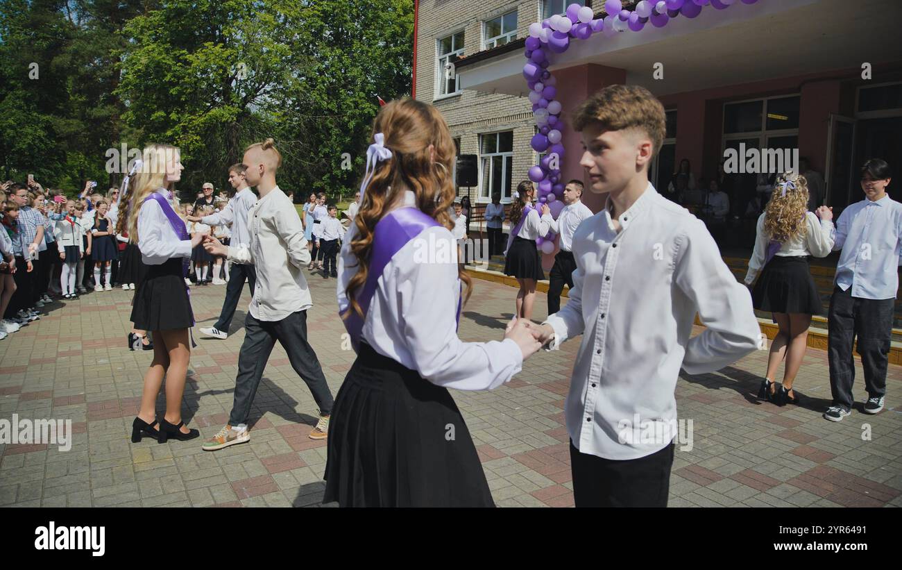 Graduates wearing sashes are dancing waltz in the schoolyard during ...