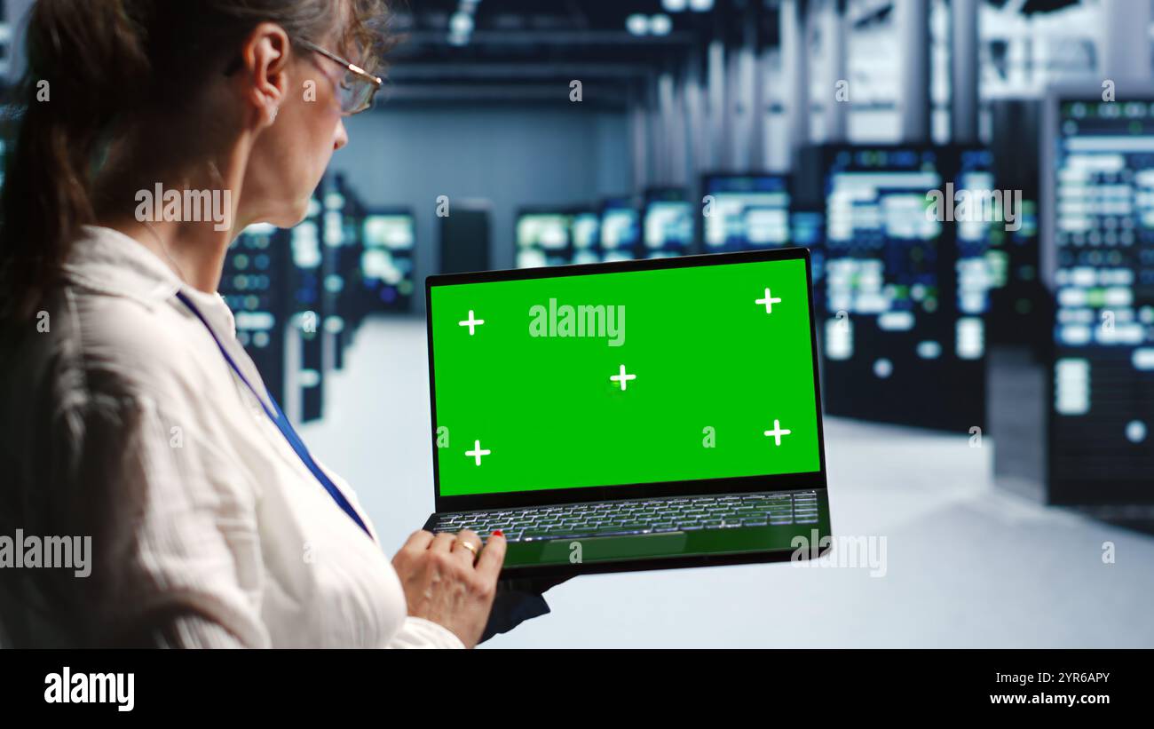 Aged technician in servers center housing high end processors capable of quickly and efficiently performing complex computations and data analysis, using mockup laptop to mend glitches Stock Photo