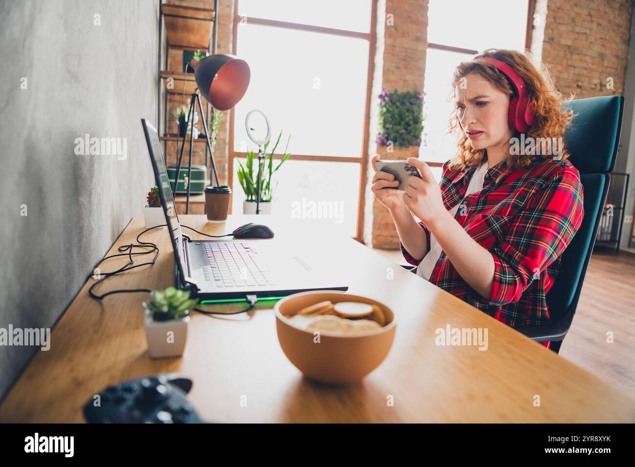 Woman immersed in mobile gaming at home workspace Stock Photo