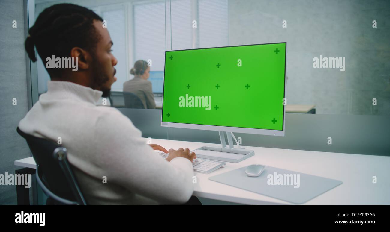 Professional African American financial expert or marketing specialist works on personal computer with green screen chromakey. Mock up template for screen content. Modern office of E-commerce company. Stock Photo