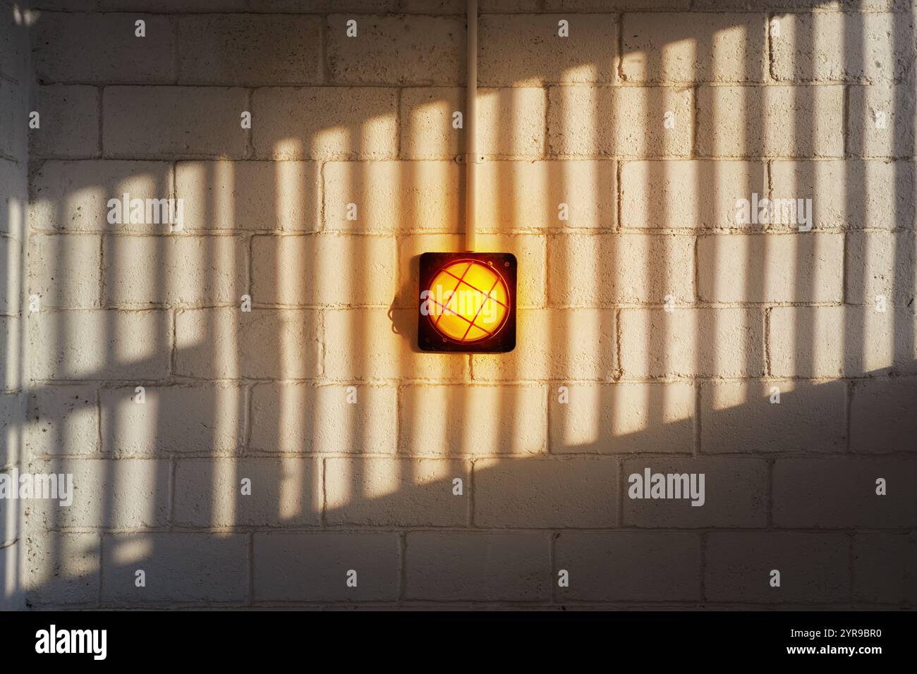A yellow wall lamp on a brick wall with a patterned shadow Stock Photo