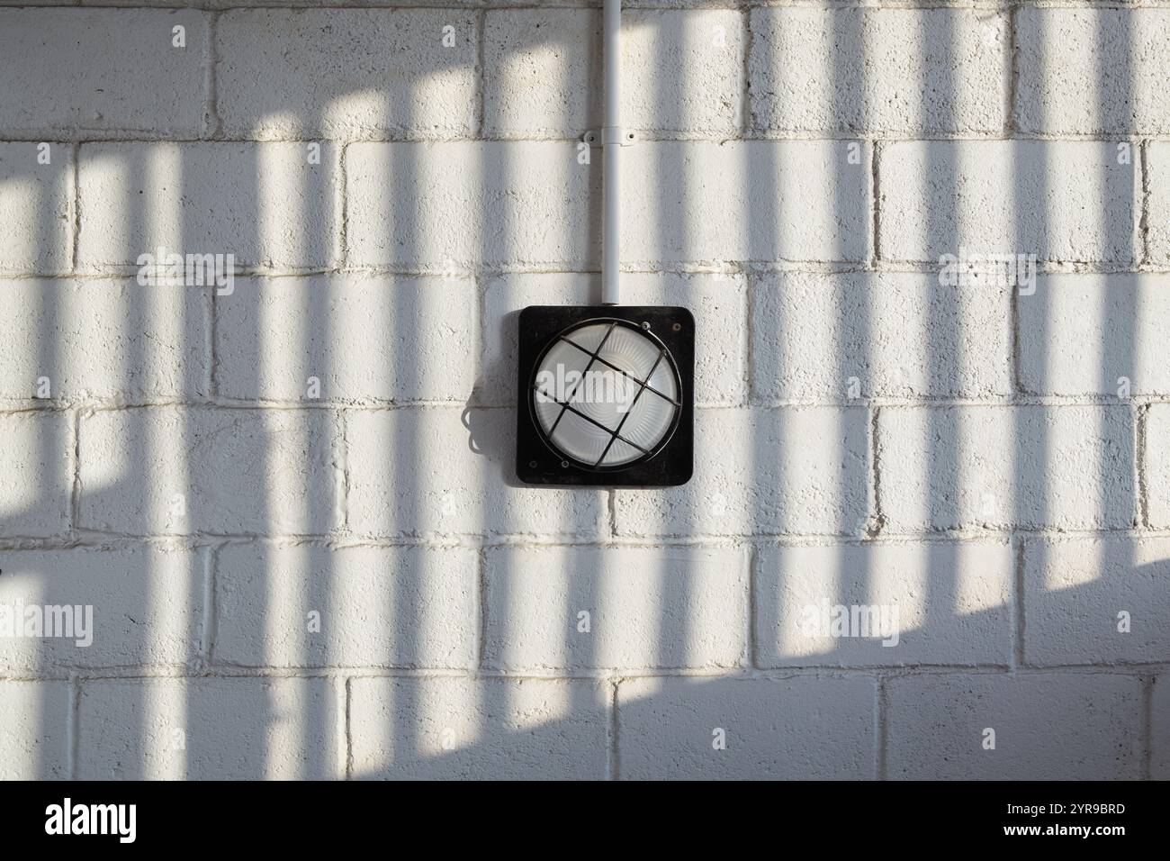 A wall lamp on a brick wall with a patterned shadow Stock Photo