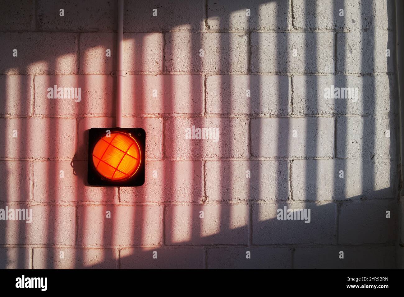 A red wall lamp on a brick wall with a patterned shadow Stock Photo