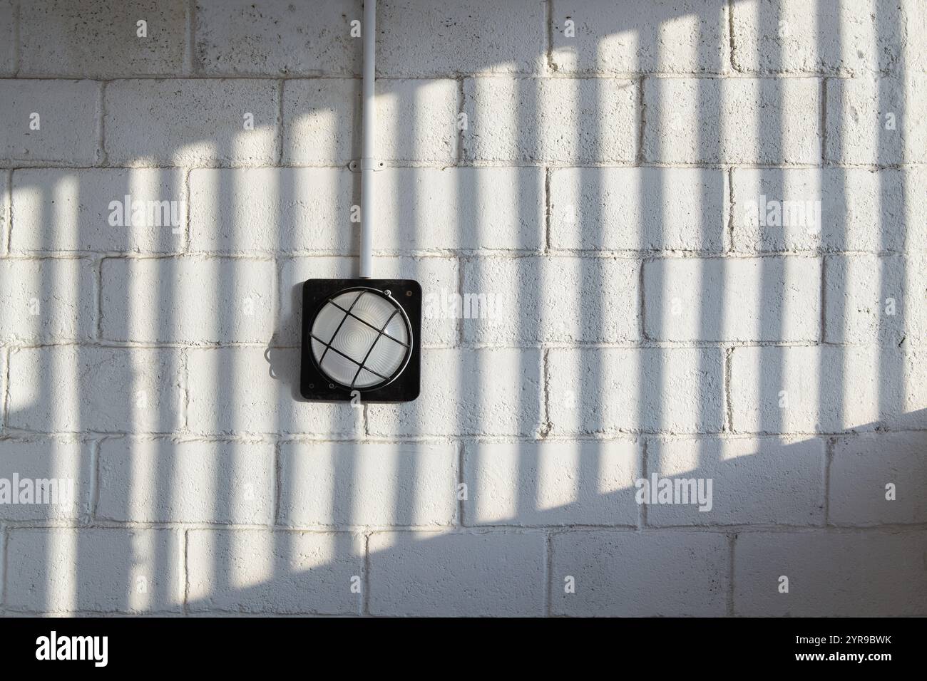 A wall lamp on a brick wall with a patterned shadow Stock Photo