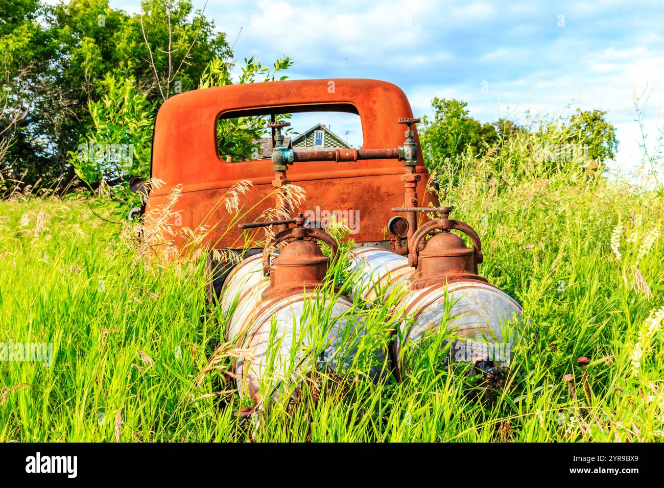 An old rusty truck is parked in a field of grass. The truck is ...