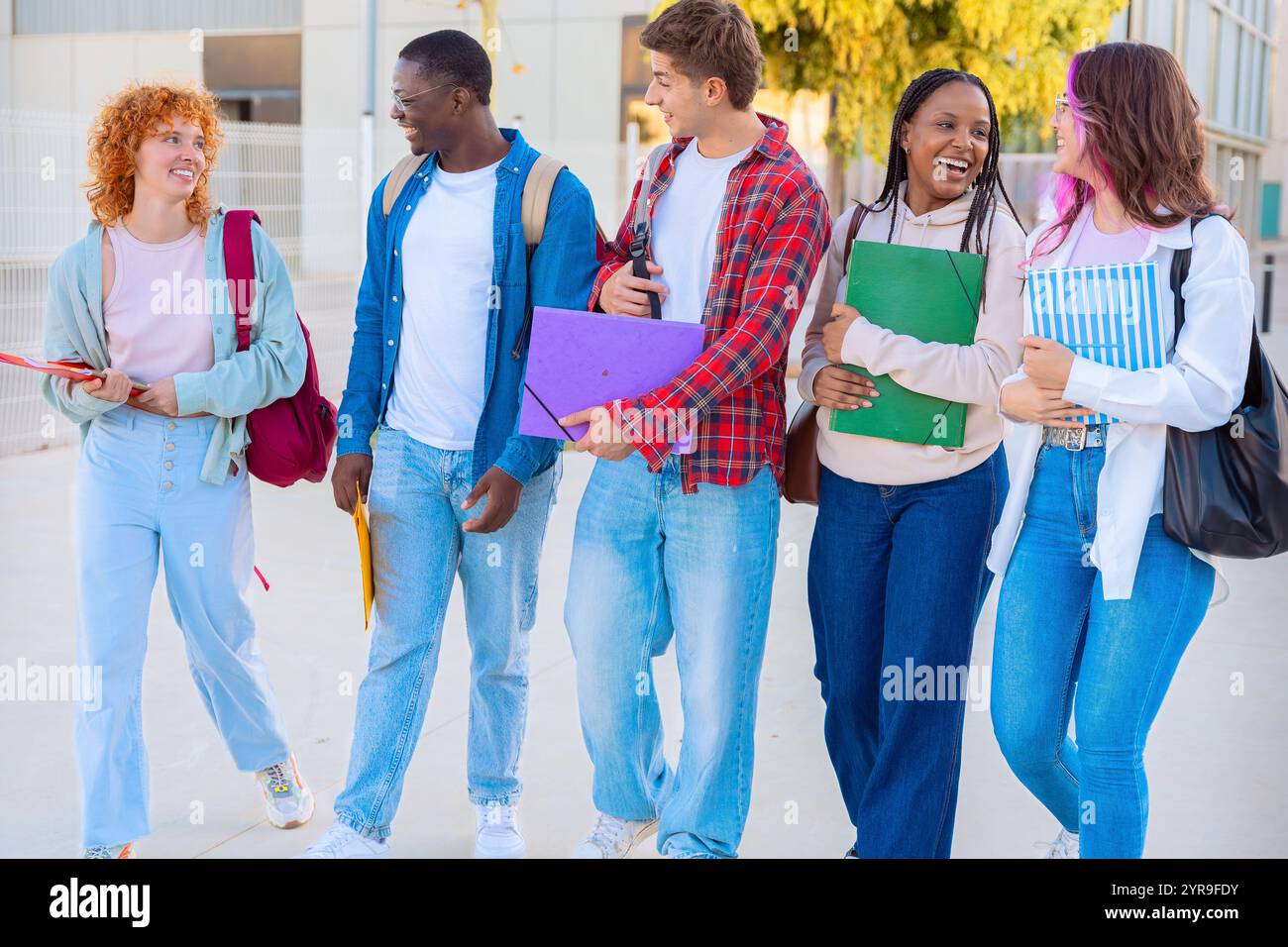 Group diverse students walking together with notebooks outdoors on a sunny day Stock Photo