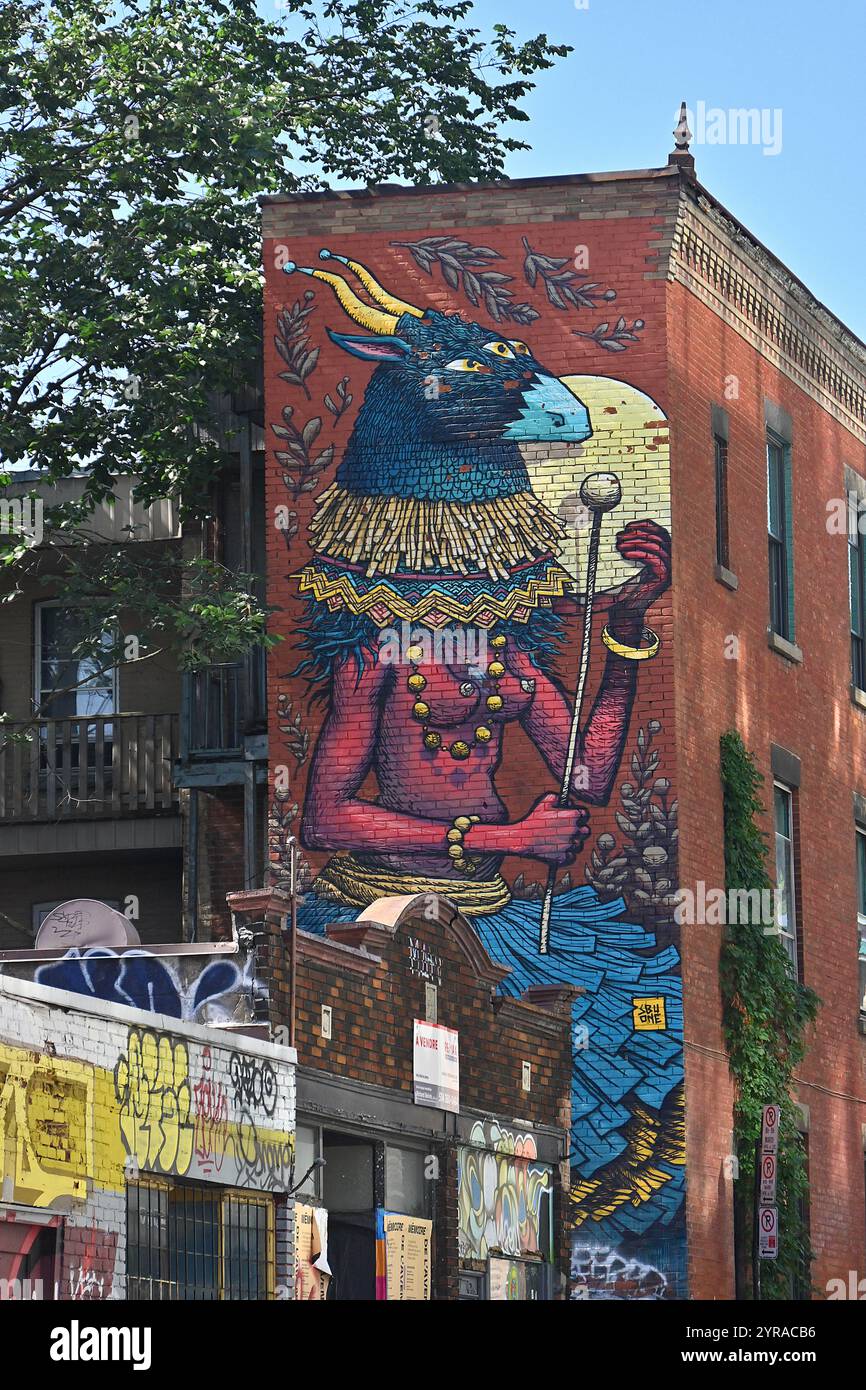 Canada, Quebec, Montreal: street art. Fresco of a woman wearing a horned animal mask by artist Sbu One on a building with red brick walls as part of t Stock Photo