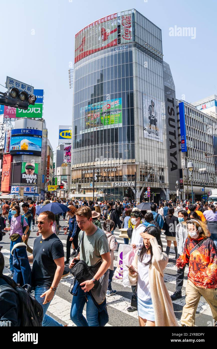 crowds of people crossing the famous Shibuya scramble crossing in the bright springtime sunshine with the landmark Tsutaya store behind them. Blue sky Stock Photo