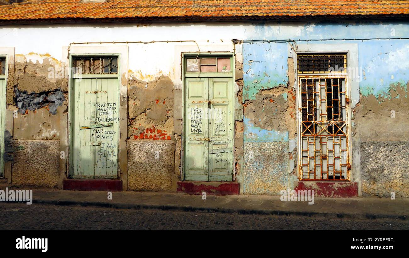 A captivating row of rustic doors on a weathered wall in Cape Verde. The faded paint and graffiti reflect a blend of history, artistry, and local life. Stock Photo