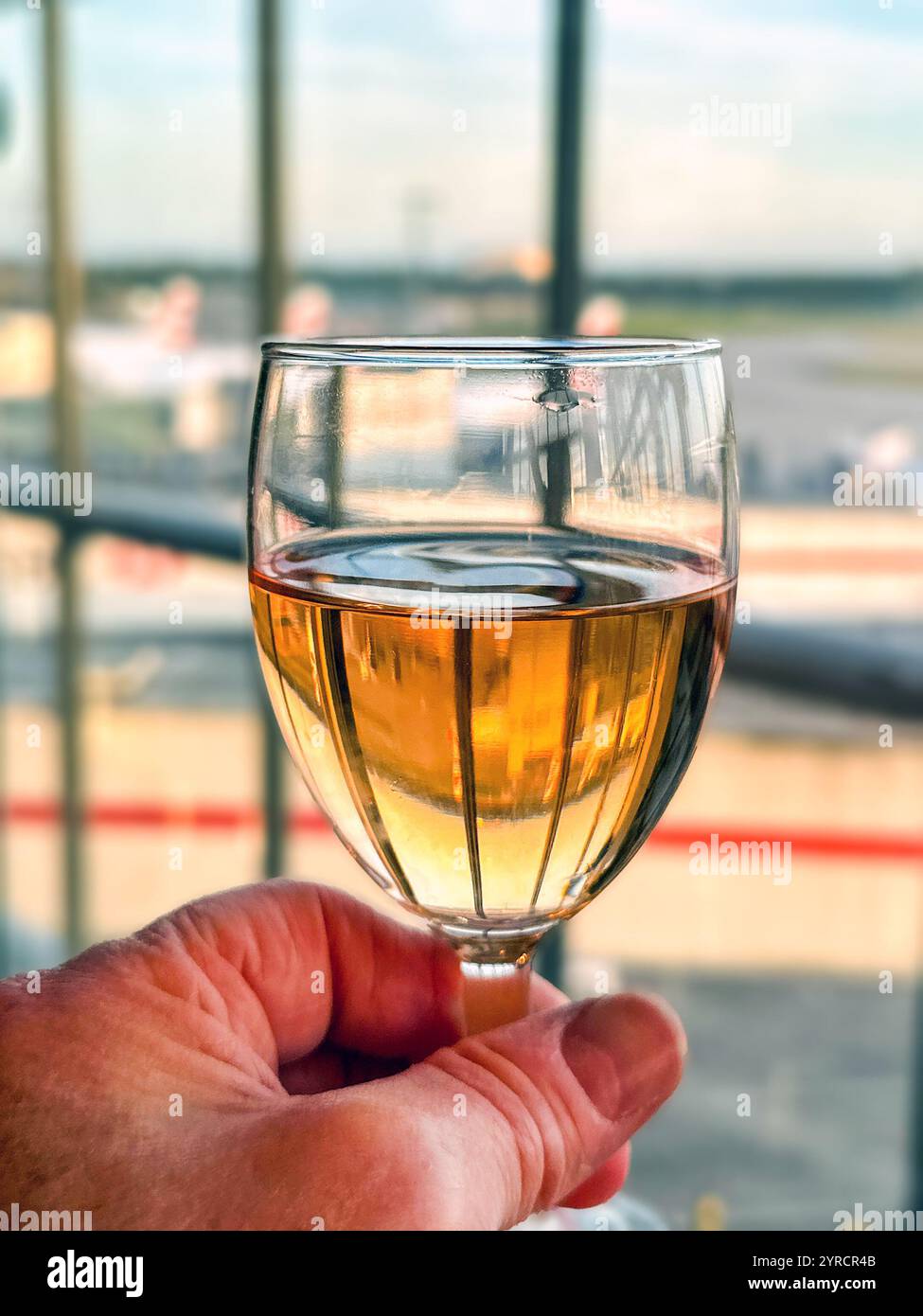 Glass of rose wine being held up in front of a window in the business lounge of an airport - Smartphone Captured Stock Image